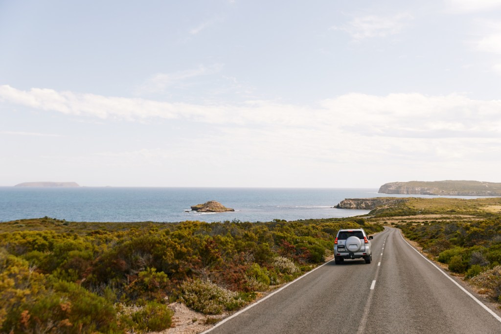 a car driving down a sealed road on top of cliffs by the seaside